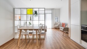 A modern living room with a dining area, featuring a wooden table and chairs, a sofa, a TV, and a kitchen area with cabinets and a stove. - GuestReady Essential - The Gods: Baldur (Porto)