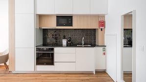 A modern kitchen with white cabinetry, a black countertop, a microwave, a stove, and a sink. - GuestReady Essential - The Gods: Baldur (Porto)