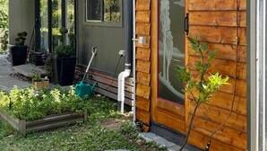 Una cabaña de madera con puerta de vidrio, un porche con plantas en macetas y un camino de piedra.