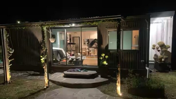 Una casa moderna con puerta de cristal, un camino de piedra y una pequeña zona de estar al aire libre.