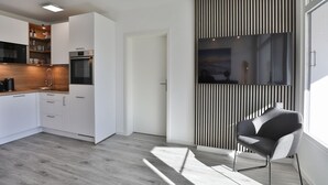 A modern kitchen with white cabinets, a wooden countertop, and stainless steel appliances. There is a black and white striped partition and a gray chair in the living area. - Strandkoje 104 - Holiday apartment near the beach in Scharbeutz - Modern, quiet & sunny (Scharbeutz)