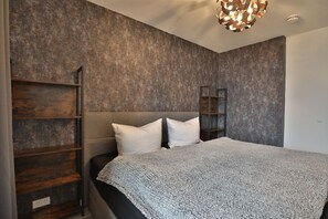 A modern bedroom with a large bed, wooden shelves, and a unique ceiling light fixture. - Strandkoje 104 - Holiday apartment near the beach in Scharbeutz - Modern, quiet & sunny (Scharbeutz)
