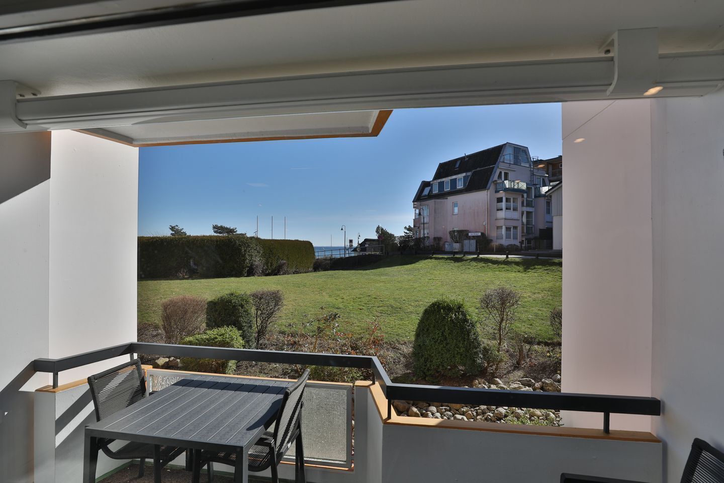 Un balcon avec une table et des chaises, donnant sur un espace verdoyant et un immeuble à plusieurs étages.