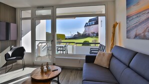 A modern living room with a sofa, a round wooden table, and a TV mounted on the wall. - Strandkoje 104 - Holiday apartment near the beach in Scharbeutz - Modern, quiet & sunny (Scharbeutz)