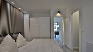 A modern bedroom with a large bed, a wardrobe, and a view into the dining area. - Strandkoje 105 - Modern vacation apartment in Scharbeutz - Close to the beach, quiet & sunny (Scharbeutz)