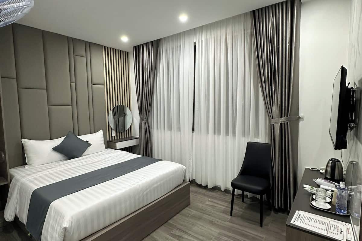 A modern hotel room with a large bed, a desk, a chair, and a TV.