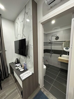 Un baño moderno con tocador de mármol, ducha con cabezal de ducha manual y televisor montado.
