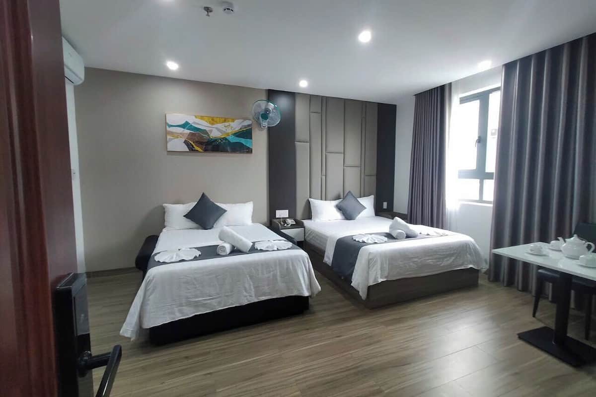 A hotel room with two beds, a desk with a chair, a ceiling fan, and a painting on the wall.