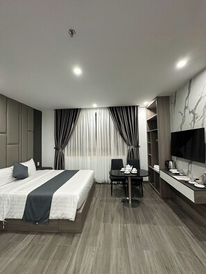 A modern hotel room with a bed, a desk, a chair, a TV, and a coffee machine.