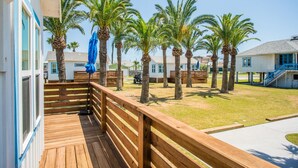 Una terraza de madera con vista a palmeras y un edificio con puerta azul.