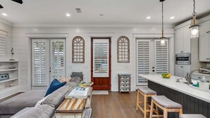 A modern kitchen with white cabinetry, a central island with stools, and a dining area with a sofa and a coffee table. - 65 Water Oak Way-Ocean Oaks (Jekyll Island)