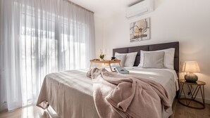 Une chambre à coucher bien rangée, avec un grand lit, une table de chevet avec une lampe et une fenêtre ornée de rideaux légers.