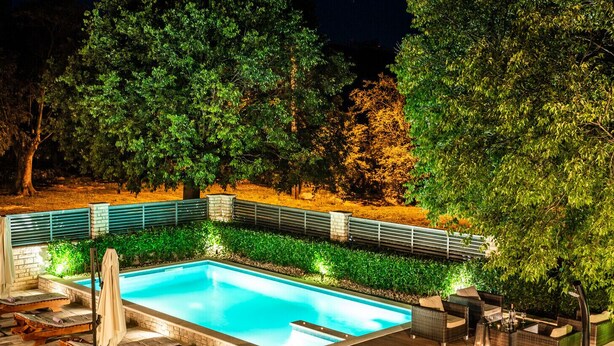 Une piscine rectangulaire bordée de pierres, entourée d’une terrasse en bois et de chaises longues.