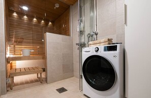 Laundry room with washing machine, wooden bench, and glass shower enclosure.