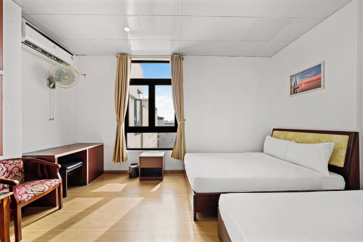 Een hotelkamer met een bed, een bureau, een stoel, een klein tafeltje en een raam met gordijnen.