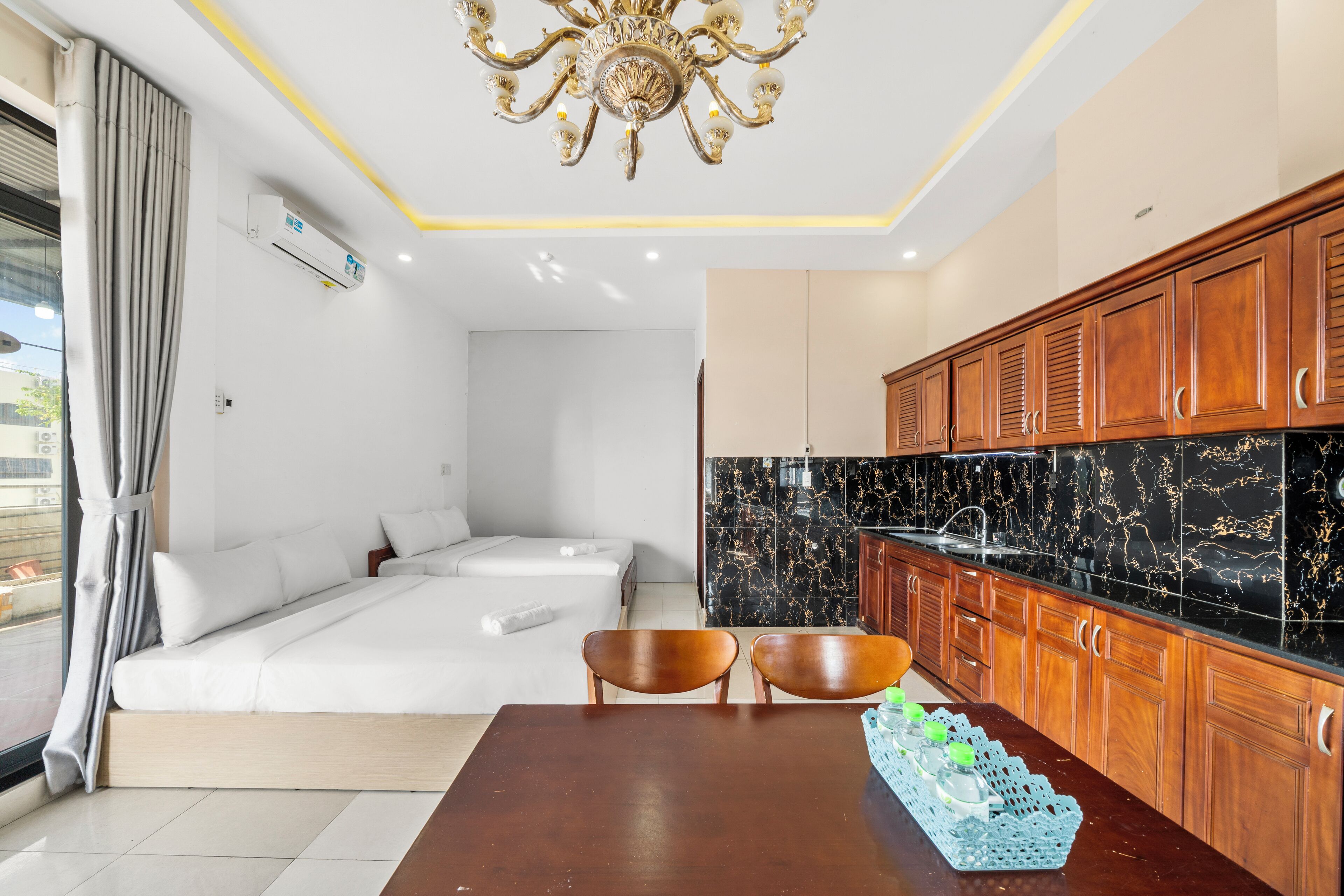 Ein modernes Hotelzimmer mit Schlafsofa, Esstisch mit Stühlen, einer Küche mit Holzschränken und einer Kristallleuchter.