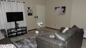 A living room with a sofa, a coffee table, a TV, and a door. - Urban Oasis in the Heart of OKC (Oklahoma City)