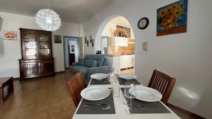 A dining area with a white table set for four, a blue sofa in the background, and a chandelier above. - PIETRA MARINA APARTMENT (BALESTRATE)