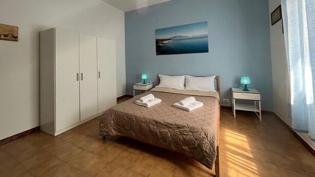 A bedroom with a bed, two bedside tables, a wardrobe, a hanging light fixture, and a painting on the wall. - PIETRA MARINA APARTMENT (BALESTRATE)