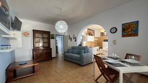 A spacious living area with a dining table set for four, a blue sofa, and a kitchen visible through an archway. - PIETRA MARINA APARTMENT (BALESTRATE)