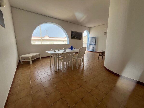 A spacious room with a dining table and chairs, a bench, and a large window offering a view of the outside. - PIETRA MARINA APARTMENT (BALESTRATE)