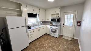 Une cuisine de taille réduite avec des meubles blancs, un réfrigérateur, une cuisinière et un four à micro-ondes.