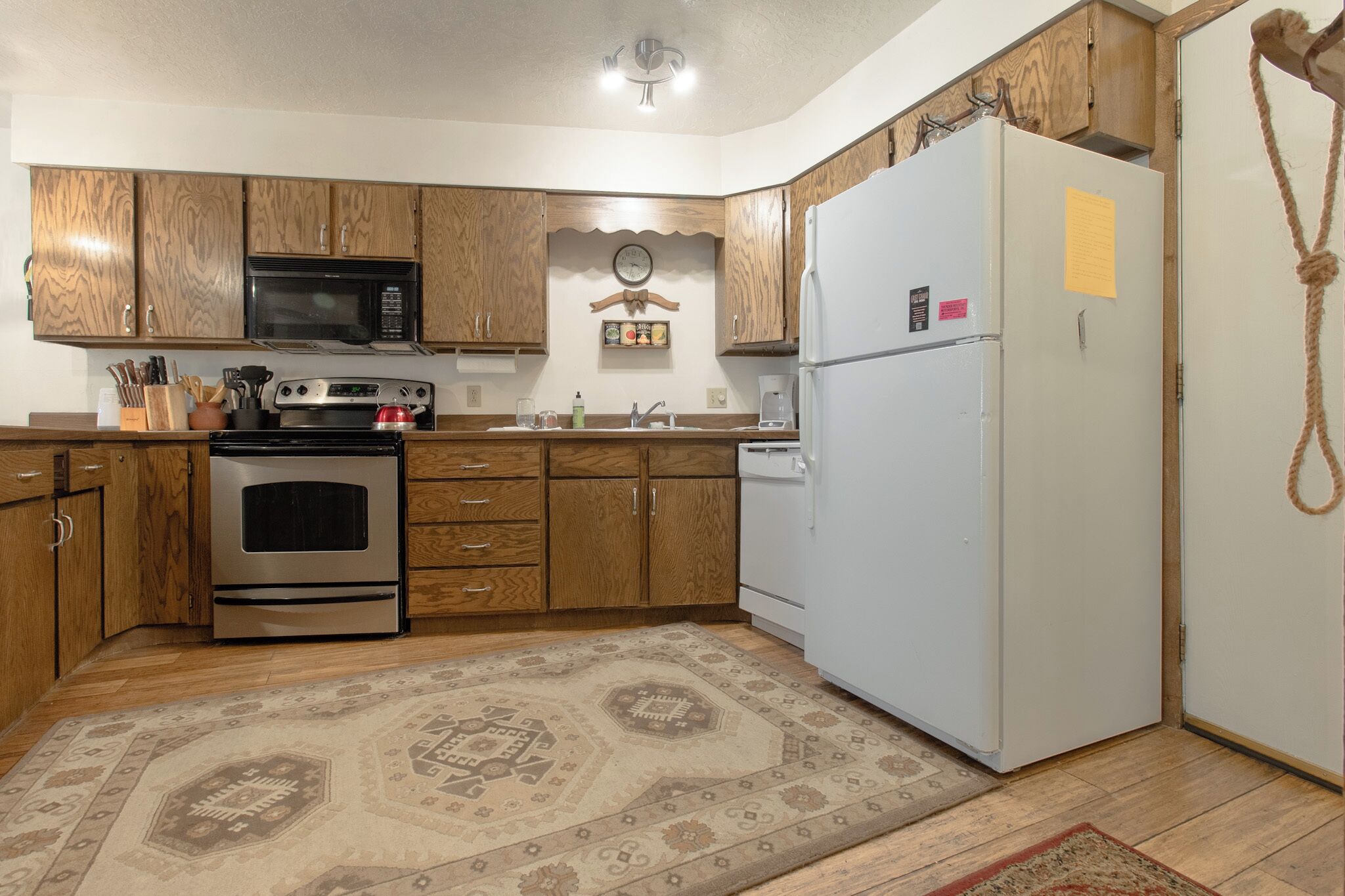 A kitchen with wooden cabinets, a stainless steel oven, a microwave, a white refrigerator, and a patterned rug.