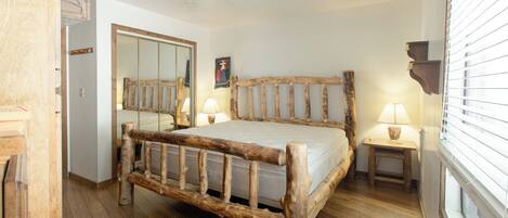 A rustic wooden bed with a headboard, a bedside table with a lamp, and a large mirror on the wall.
