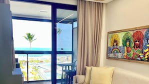 A modern living room with a sofa, a chair, a painting, and a view of the ocean.