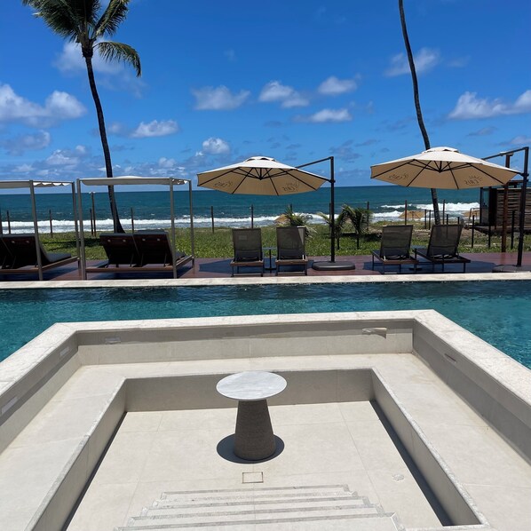 A poolside area with lounge chairs and umbrellas, overlooking the ocean.