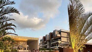 A modern building with a sign that reads "CAIS ECO RESIDÊNCIA" surrounded by greenery and palm trees.