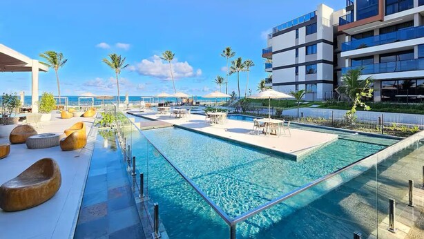 A rooftop pool area with clear blue water, lounge seating, and a view of the ocean.