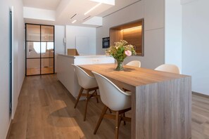 A modern kitchen with a wooden island, white chairs, and a vase of flowers. - Luxurious Apartment With Stunning sea View (Middelkerke)