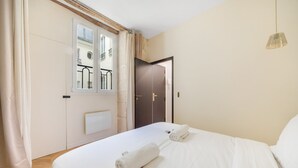 A hotel room with a bed, two rolled towels, a window with a view of a balcony, and a door. - Paris Marais City Heart (Paris)