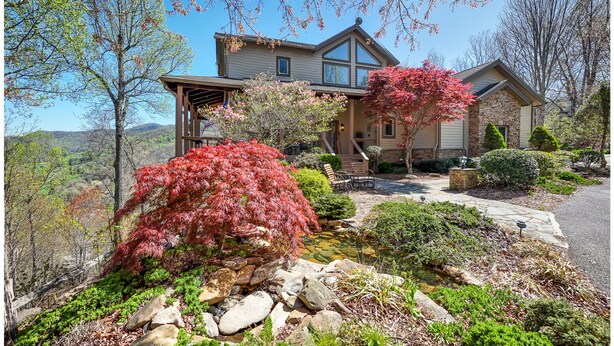 A two-story house with a stone facade, a covered porch, and a landscaped garden with a pond.