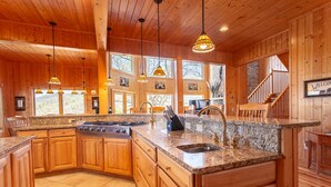 A spacious kitchen with granite countertops, wooden cabinets, and a central island with a sink and stove.