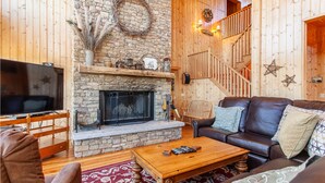 A cozy living room with a stone fireplace, wooden walls, a leather sofa, and a flat-screen TV.