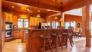 A spacious kitchen with wooden cabinets, a large island with bar stools, and a ceiling fan.