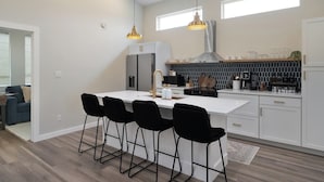 Ett modernt kök med en central köksö, barstolar, en fläktkåpa i rostfritt stål och ett stänkskydd med hexagonformade kakelplattor.