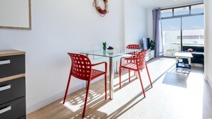 A modern room with a glass dining table, red chairs, a small potted plant, and a view of the city through large windows.