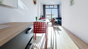 A modern, well-lit room with a dining area featuring a glass table, red chairs, and a blue sofa. A lifebuoy hangs on the wall, and there are potted plants on the table.