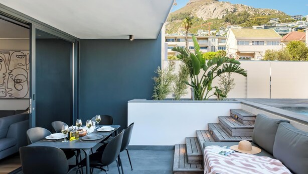 A modern outdoor dining area with a table set for two, a sofa, and a view of a mountain. - Modern Central Secure Cape Town 2bed Bantry Suite (Cape Town)