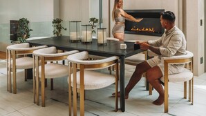 A modern dining area with a long table, cushioned chairs, and pendant lighting.