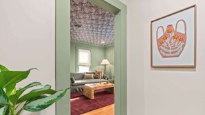 Un pasillo con pared verde, suelo de madera, un sofá, una mesa de centro y una planta.