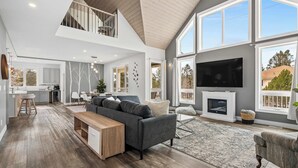 A spacious living area with a large gray sofa, a wooden coffee table, and a fireplace. - Radiant Retreat | Sleeps 13 + Loft | Stunning View (Radium Hot Springs)