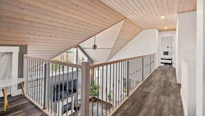 A modern interior with a wooden ceiling, a balcony with a railing, and a staircase leading to an upper level. - Radiant Retreat | Sleeps 13 + Loft | Stunning View (Radium Hot Springs)