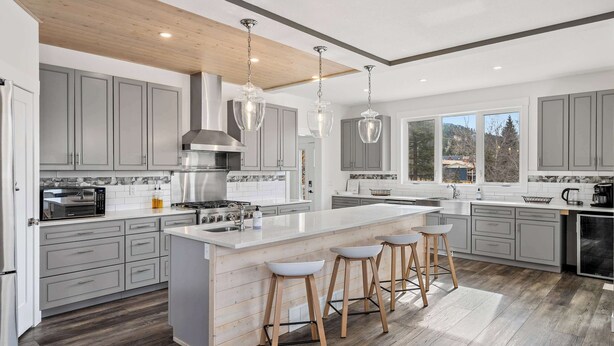 A modern kitchen with grey cabinets, a large island with stools, stainless steel appliances, and a wooden ceiling. - Radiant Retreat | Sleeps 13 + Loft | Stunning View (Radium Hot Springs)