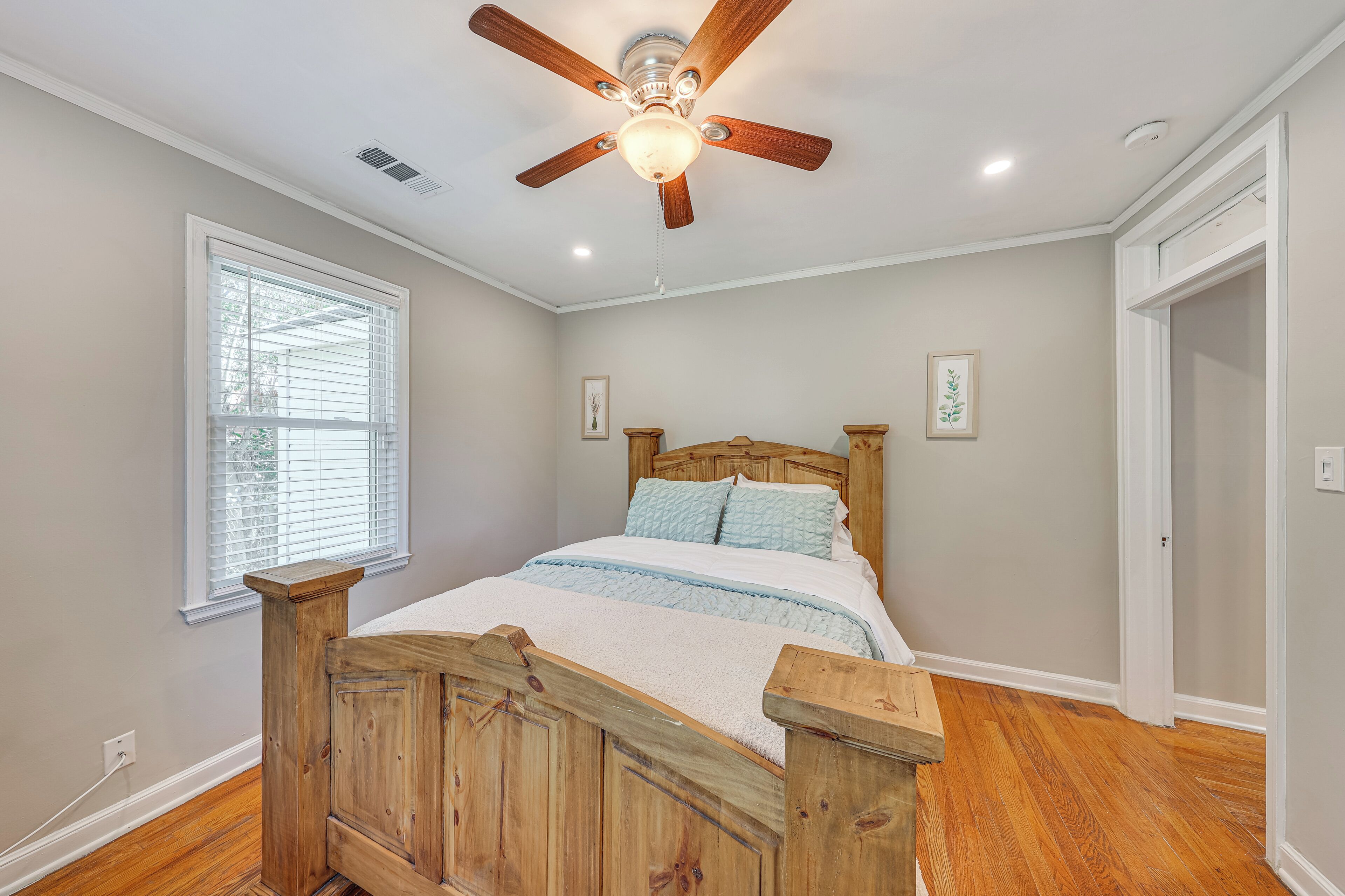 A bedroom with a wooden bed, a ceiling fan, a window with blinds, and a door.