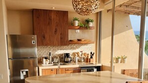 A kitchen with a central island, wooden cabinets, a stainless steel refrigerator, and a hanging light fixture. - Elegant Oceanview Suite Perfect Hideaway for two (La Majahua)