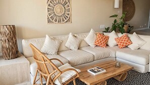 A living room with a white sofa, a wooden coffee table, a wicker chair, a black and white patterned rug, a ceiling fan, and a wall-mounted air conditioner. - Elegant Oceanview Suite Perfect Hideaway for two (La Majahua)